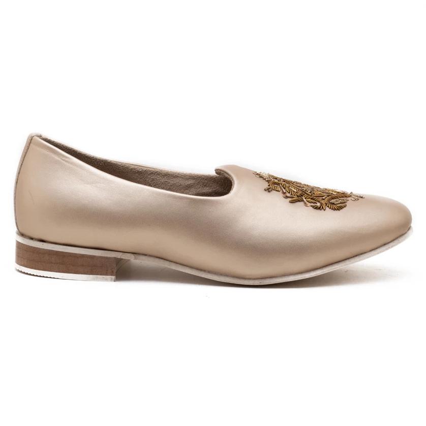 A pair of Monkstory Magenta Mojri - Cream shoes with a gold embroidered crest.