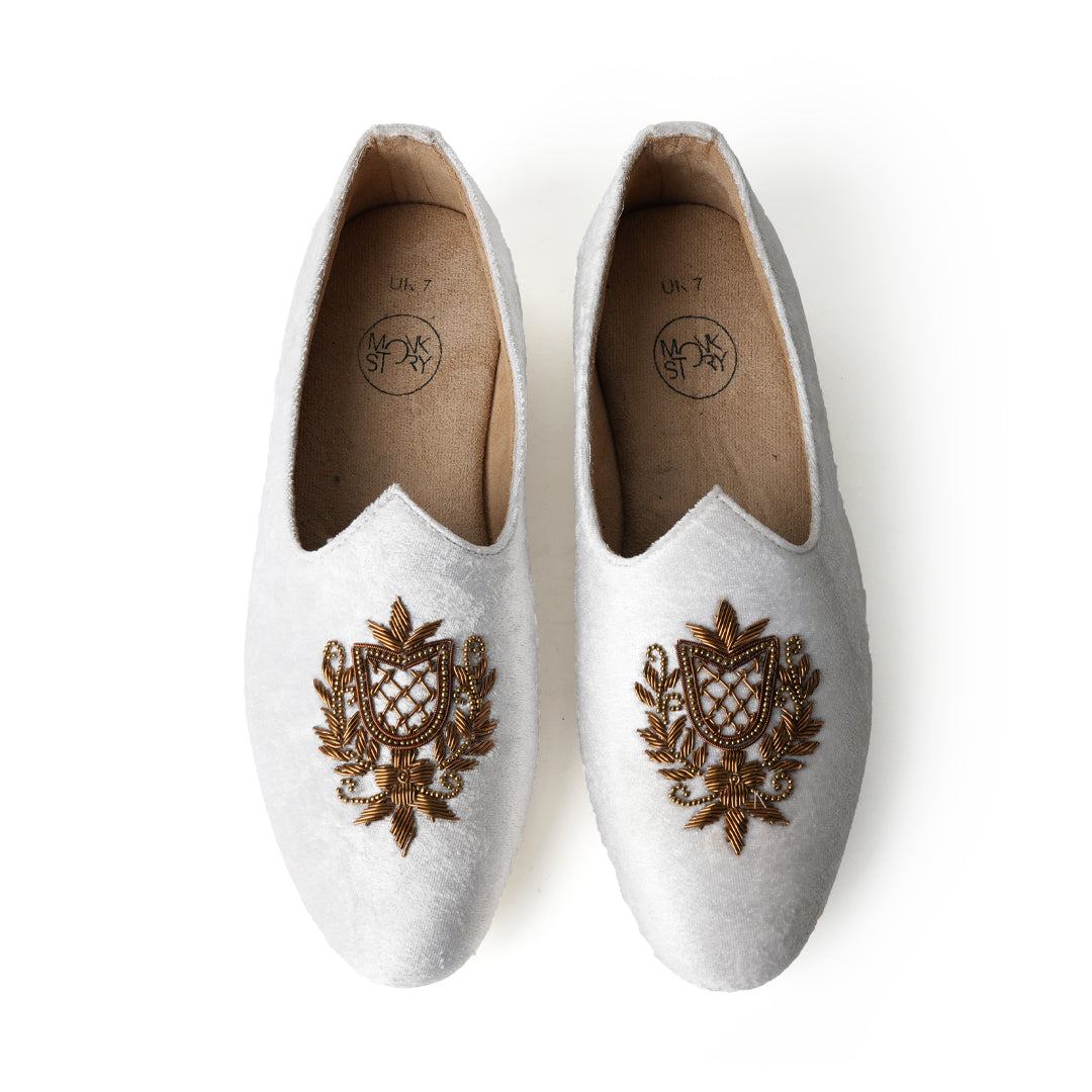 A pair of timeless white Opulenza Embroidered Mojri slippers with hand-embroidered gold motifs by monkstory.