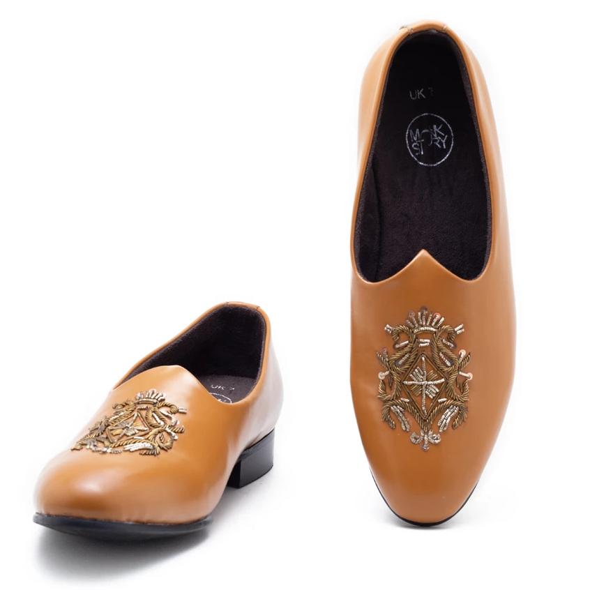 A pair of Magenta Mojri - tan loafers with a hand-embroidered crest by Monkstory.