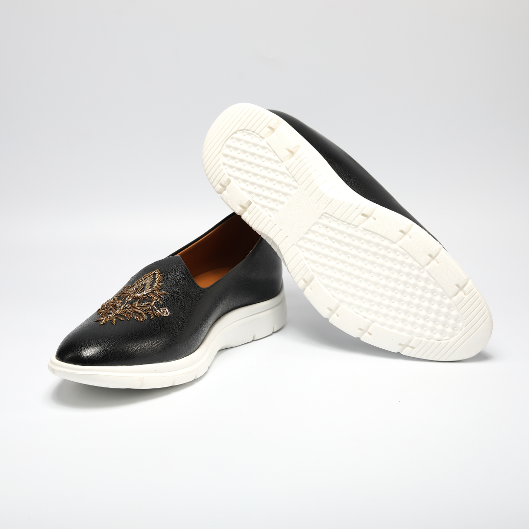 A black leather slip on shoe with gold embroidery, perfect for ethnic wear.