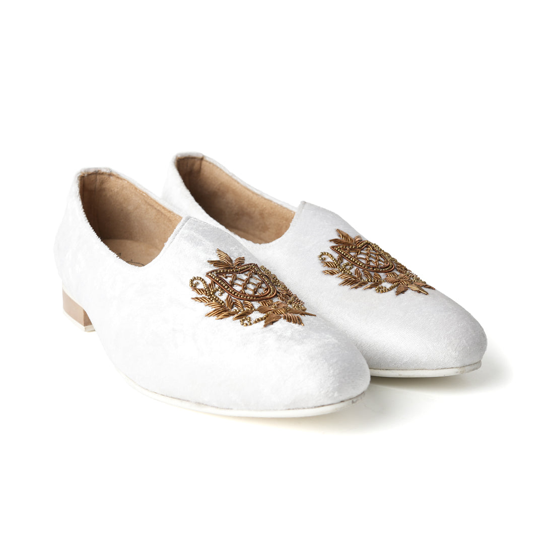 A pair of timeless white Opulenza Embroidered Mojri slippers with hand-embroidered gold motifs by monkstory.